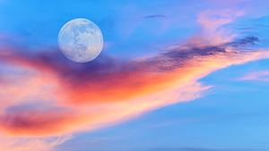 Vollmond am blauen Himmel hinter bunten Wolken - Foto: David Baileys / iStock