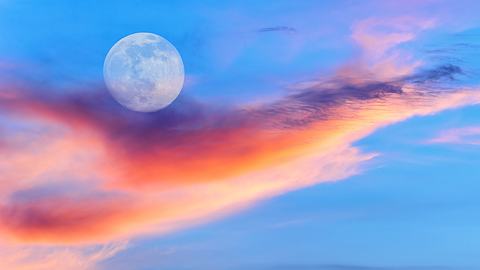 Vollmond am blauen Himmel hinter bunten Wolken - Foto: David Baileys / iStock