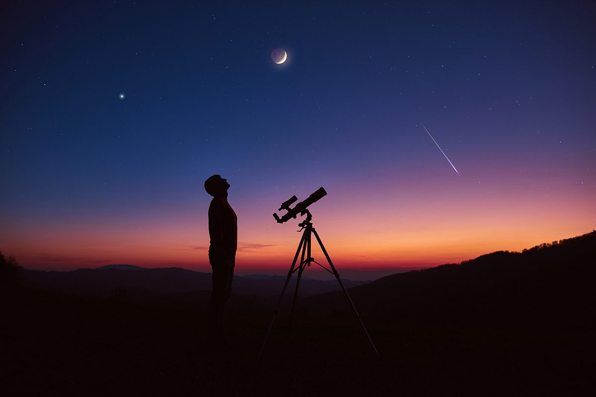 Mann schaut mit dem Sternengucker in den Nachthimmel zu einer Mondfinsternis