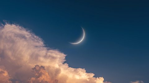 Neumond steht von Wolken umgeben am blauen Himmel umgeben - Foto: Nazarii Neshcherenskyi / iStock