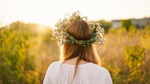 Eine Frau mit Blumenkranz im Haar blickt zur Sonne - Foto: Anastasiia Stiahailo/iStock