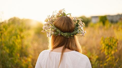 Eine Frau mit Blumenkranz im Haar blickt zur Sonne - Foto: Anastasiia Stiahailo/iStock